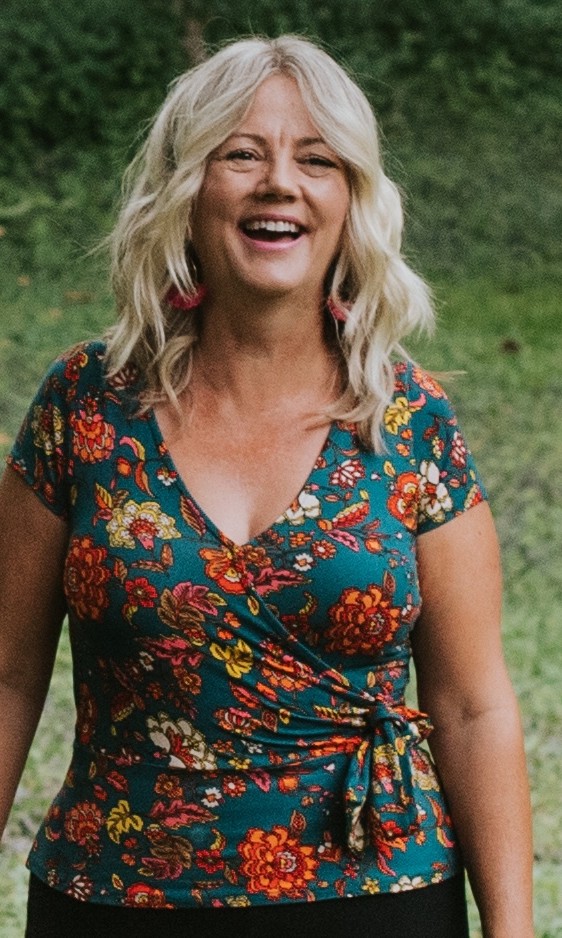 Sonya laughing outdoors in a colourful floral top and red tassel earrings