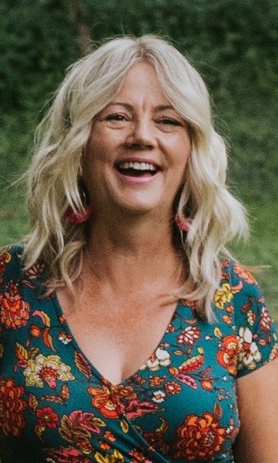 Sonya laughing outdoors in a colourful floral top and red tassel earrings